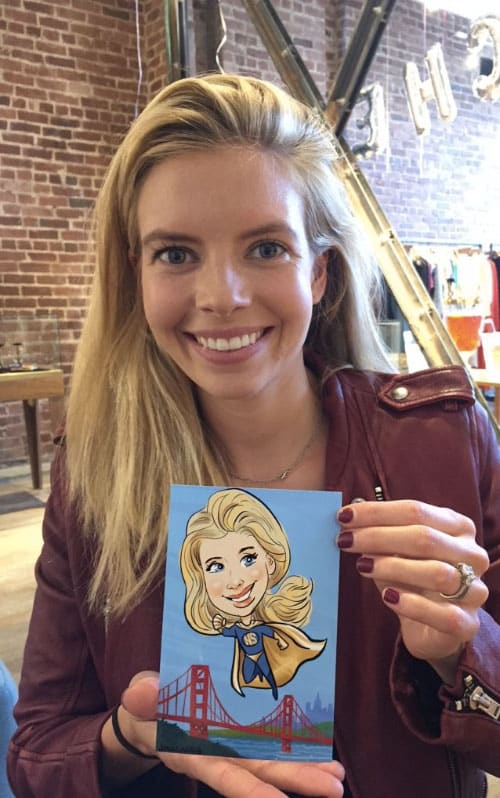 Smiling woman holding her custom superhero caricature, featuring a cape and the San Francisco Bay Golden Gate Bridge in the background